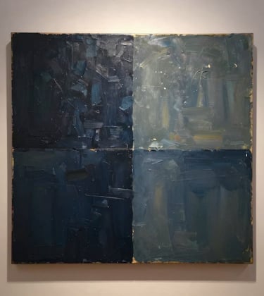 A close-up photograph of a contemporary oil painting featuring textured strokes of dark navy and muted blue-grey, illuminated by a warm spotlight in an international gallery setting.