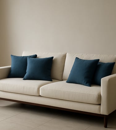 A minimalist home sofa in off-white fabric with steel blue cushions, set against a clean wall in a modern South Asian living room with soft natural lighting.