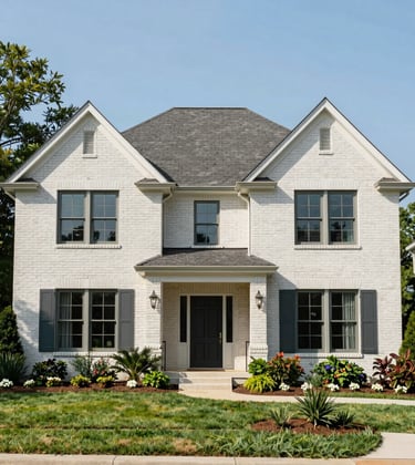 An elegant brick traditional home with manicured landscaping and a vibrant garden in a North American / Southern US residential neighborhood, captured in bright, clear daylight to highlight the architectural details in muted steel blue and pale misty white.
