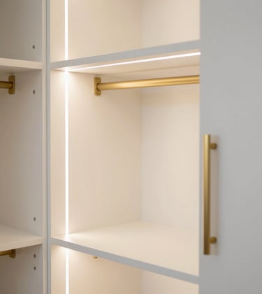 A luxury walk-in wardrobe with soft white shelving, warm integrated LED lighting, and metallic gold handle details.