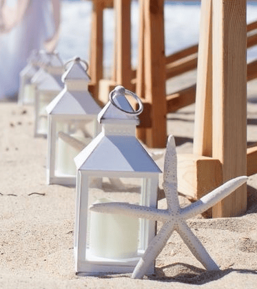 white lantern with candle set on the sand with white starfish