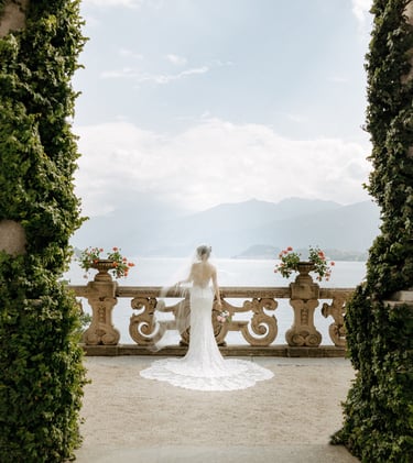 a bride in a white wedding dress standing in front of a lake at Villa Balbianello