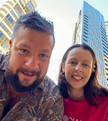 Two people smiling outdoors with modern city buildings in the background