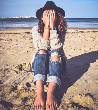 une femme qui se cache les yeux assise sur le sable