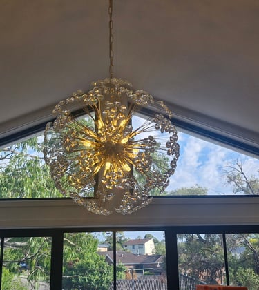 Elegant crystal sputnik chandelier hanging from a vaulted ceiling in a modern home with large windows.