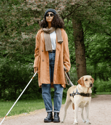 Legally blind disabled woman walking in a park with her guide dog and cane, both non optical aids