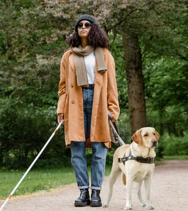 Legally blind disabled woman walking in a park with her guide dog and cane, both non optical aids