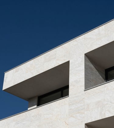 Modern architecture details of a luxury residence. Sharp angles of white stone against a navy blue sky. Professional minimalist photography focusing on the quality of materials and design.