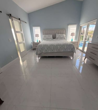 Elegant light blue bedroom with a white bed, tall ceilings, large windows, and sleek white tile flooring, perfect for a