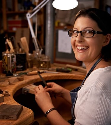 Diseñadora de joyería artesanal sonriente trabajando con herramientas manuales en su estudio