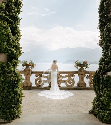 a bride in a white wedding dress standing in front of a lake at Villa Balbianello