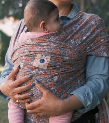 Mother holding her baby in a floral patterned ergonomic baby wrap carrier outdoors.
