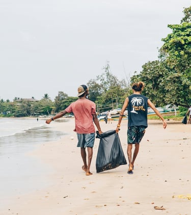 Two men walking down a beach, holding a garbage bag between them.