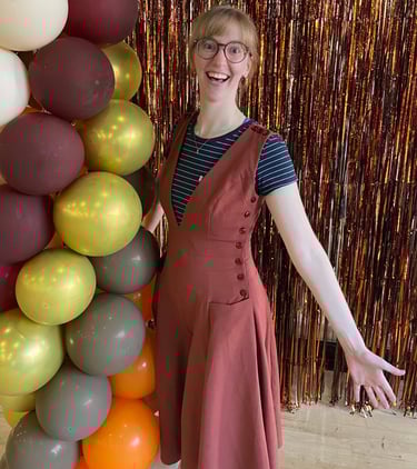 Natalie in a dress and glasses standing in front of a balloon arch