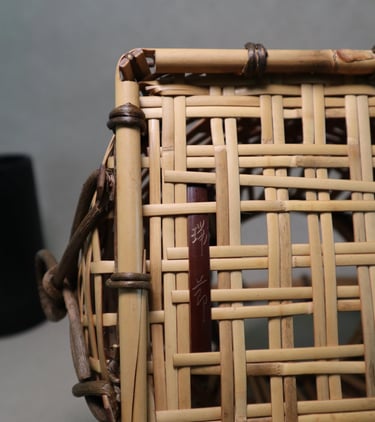 Close-up of a hand-woven Japanese bamboo basket with a dark wood signature plaque and intricate rattan bindings.