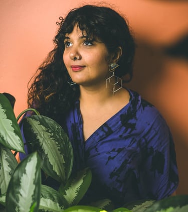 Portrait de Salima, femme à la peau brune et aux longs cheveux bouclés, entourée de plantes.