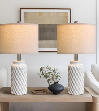 A pair of white textured ceramic table lamps with linen shades on a wooden console table.