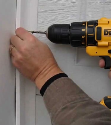 Handyman using a DeWalt cordless power drill to drive a screw into white trim for home repair.