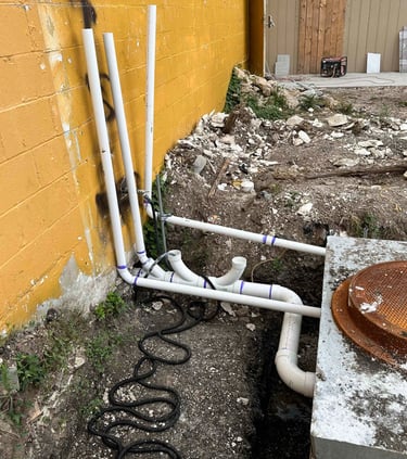 PVC plumbing pipes and a septic tank riser installed outside a yellow building wall.