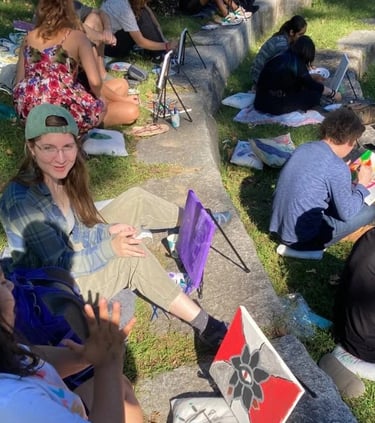A group of students painting on canvases at an outdoor art workshop in a park.