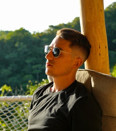 a man sitting in a hammock with sunglasses. looking at the sunset