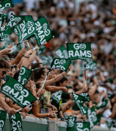 Image of several people blurred out at the stadium waving green flags that read GO RAMS.