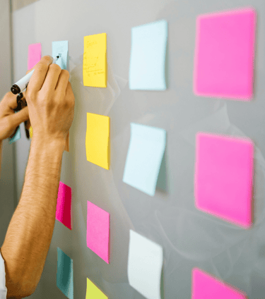 Geeltjes op whiteboard met hand en pen, symboliseert kleine stappen en flexibel beleid.