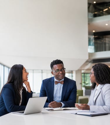 Three diverse business professionals in formal attire having a meeting at a white office table with a laptop.