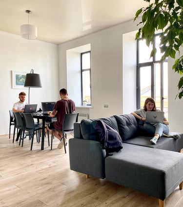 Young professionals working on laptops in a bright, modern open-plan office with a sofa and dining table.