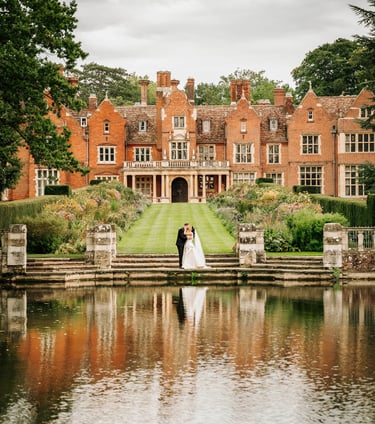 Bride and groom standing by a lake in front of a grand manor house