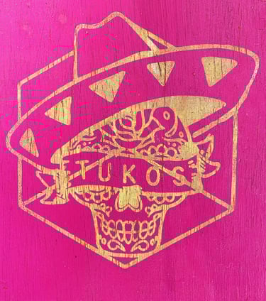a pink and gold painted wooden sign with a mexican skull