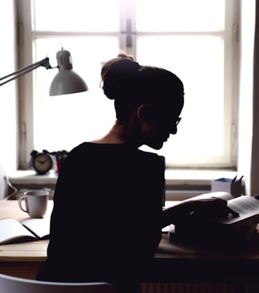 Rearview silhouette of a young woman sitting at a desk in front of a window