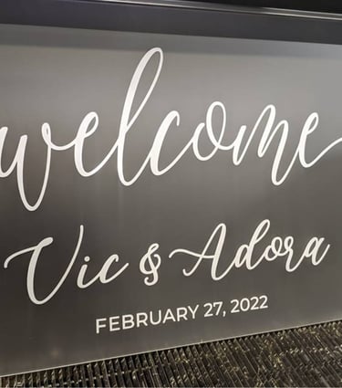 Gray acrylic welcome sign with 'Vic & Adora, February 27, 2022' in white script, ready for a wedding