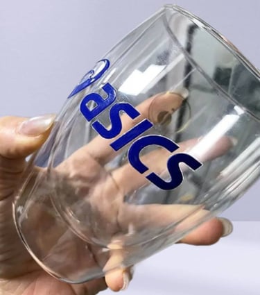 Hand holding a clear glass mug with a UV DTF printed 'Basics' sticker.