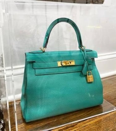 Teal designer handbag showcased in clear acrylic box.
