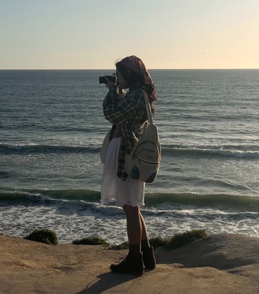 Vibey full body candid shot of me holding camera up to my face, standing on cliffs over ocean.Earthy