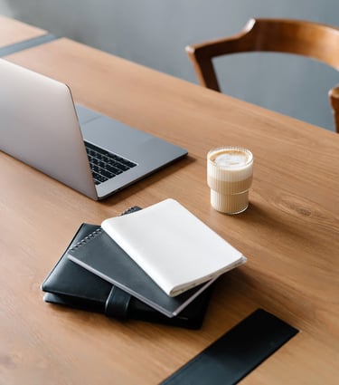 An open laptop, datebook, notebook, and coffee cup on top or a wodd desk.