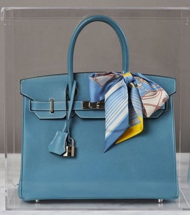 Blue luxury bag in a sleek acrylic display case.