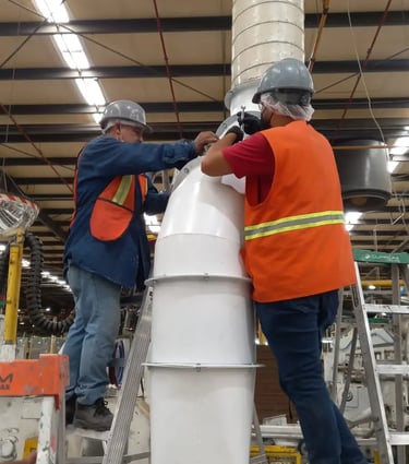 Dos trabajadores industriales con chalecos de seguridad instalando un sistema de ducto de extracción