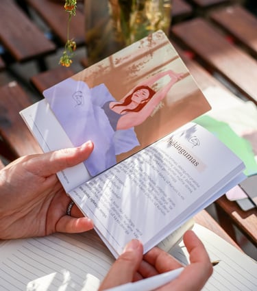 Kortelė iš "Terapiniai pokalbiai su savimi" rinkinio padėta ant knygelės, laikomos rankose