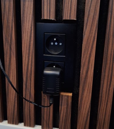 Zoom sur l'intégration de prises noires dans un panneau en lattes de bois foncé