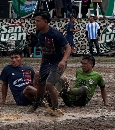 Athletes competing in a muddy soccer match on a rain-soaked field during a local tournament.