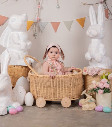 una bebé con un disfraz de conejito dentro de una carriola de paja celebrando la pascua