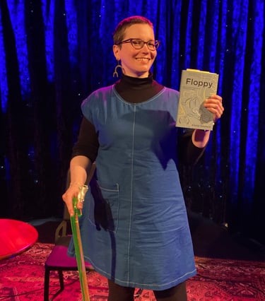 Alyssa Graybeal on stage holding Floppy. Alyssa has buzzed hair, a lime green cane, and glasses.