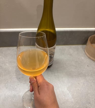 hand holding a orange looking glass of wine, with the bottle showed in the background