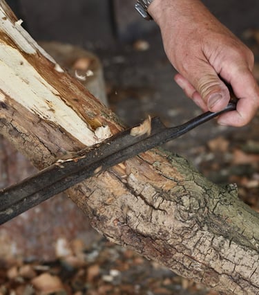 a person holding a drawknife and using it to remove bark