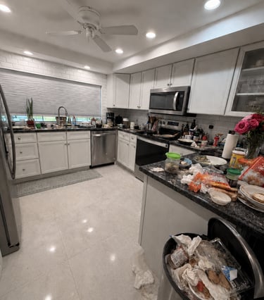 Messy modern kitchen with white cabinets, stainless appliances, and a full trash can.