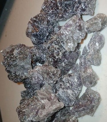 Raw chunks of dark purple and black MDMA crystals, also known as Molly, on a white surface.