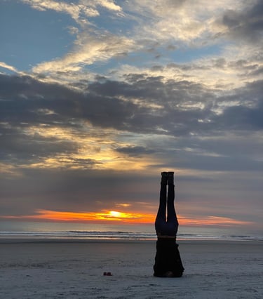 A woman doing a headstand on the beach silhouetted by the sunrise