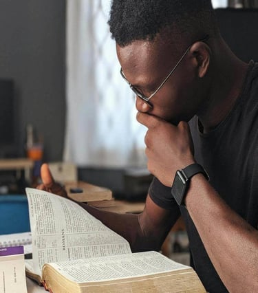 a man sitting at a desk with a bible and a laptop